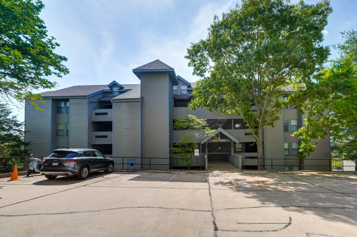 A welcoming exterior scene showing a multistory building nestled among lush, mature trees, with a parking area in front where families can gather, unload, and prepare for a day of nearby adventures. The overall atmosphere is inviting, perfect for arriving back home after a day out.