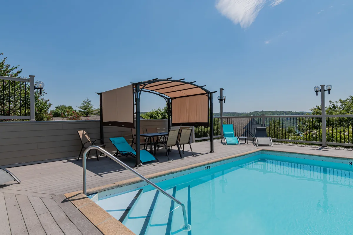 A sparkling outdoor swimming pool surrounded by comfortable lounge chairs and a canopy structure, set amid a landscaped area with open views of the surrounding hills. The tranquil atmosphere invites guests to enjoy swimming, sunbathing, or socializing outdoors.
