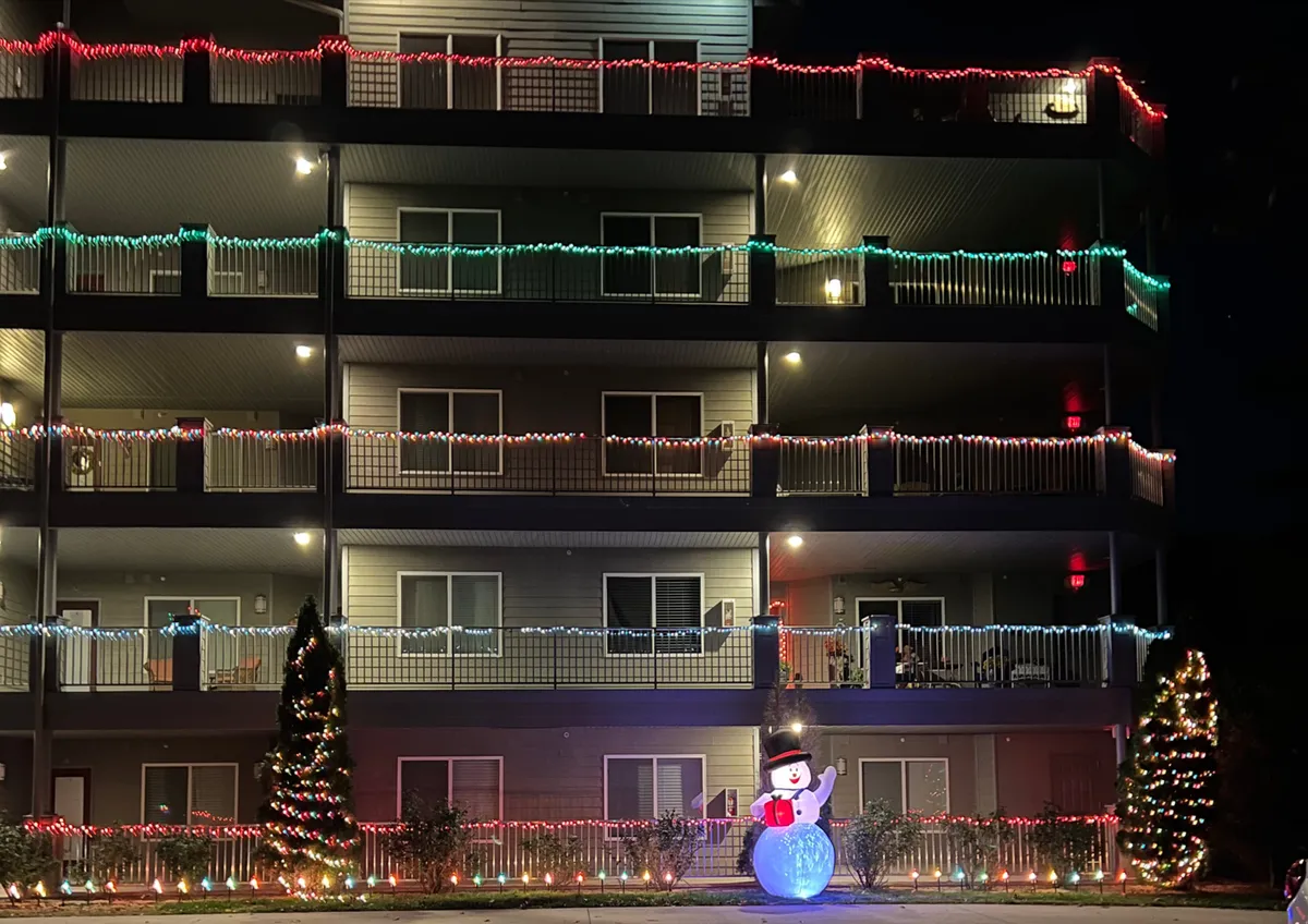 A festive exterior scene featuring decorative lights, a snowman, and a Christmas tree, all set for the holiday season. The joyful decorations suggest celebration, family gatherings, and community spirit during the cooler months.