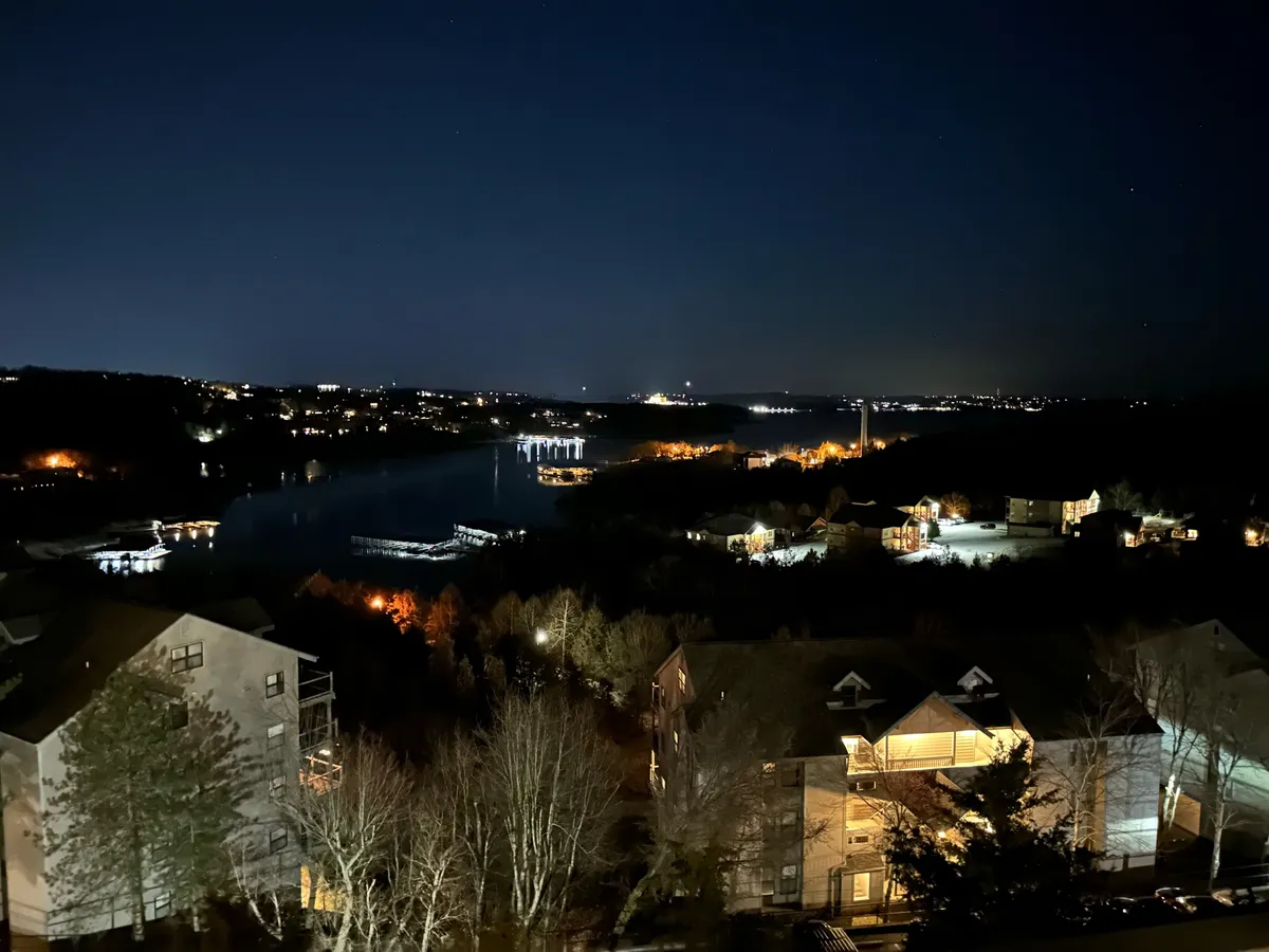 This serene view captures calm water reflecting the evening lights, with boats docked along the shore and distant hills illuminated as dusk falls. The tranquil atmosphere suggests opportunities for boating and lakeside fun during the warmer months, while also evoking peaceful moments after a day of exploration.