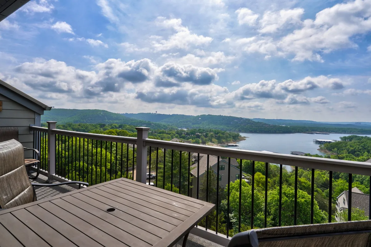 This image captures a private deck with a balcony railing, a table, and seating, overlooking panoramic views of Table Rock Lake and the rolling hills beyond. The tranquil setting is perfect for relaxing, reading, or enjoying a meal outdoors.
