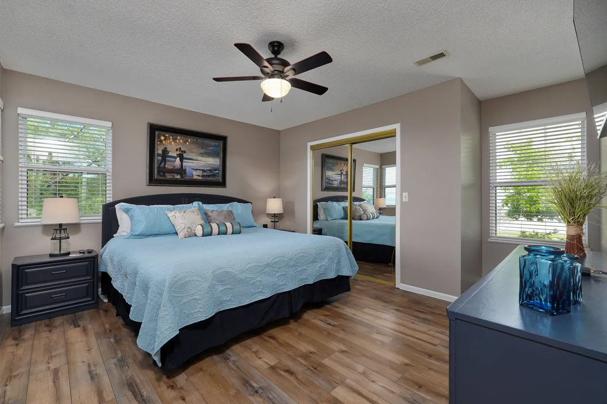 A calm, serene bedroom featuring a comfortable bed with neutral bedding, a nightstand with a lamp, wall art above the headboard, and a neatly arranged dresser. Soft natural light fills the space, creating a tranquil environment perfect for relaxation.