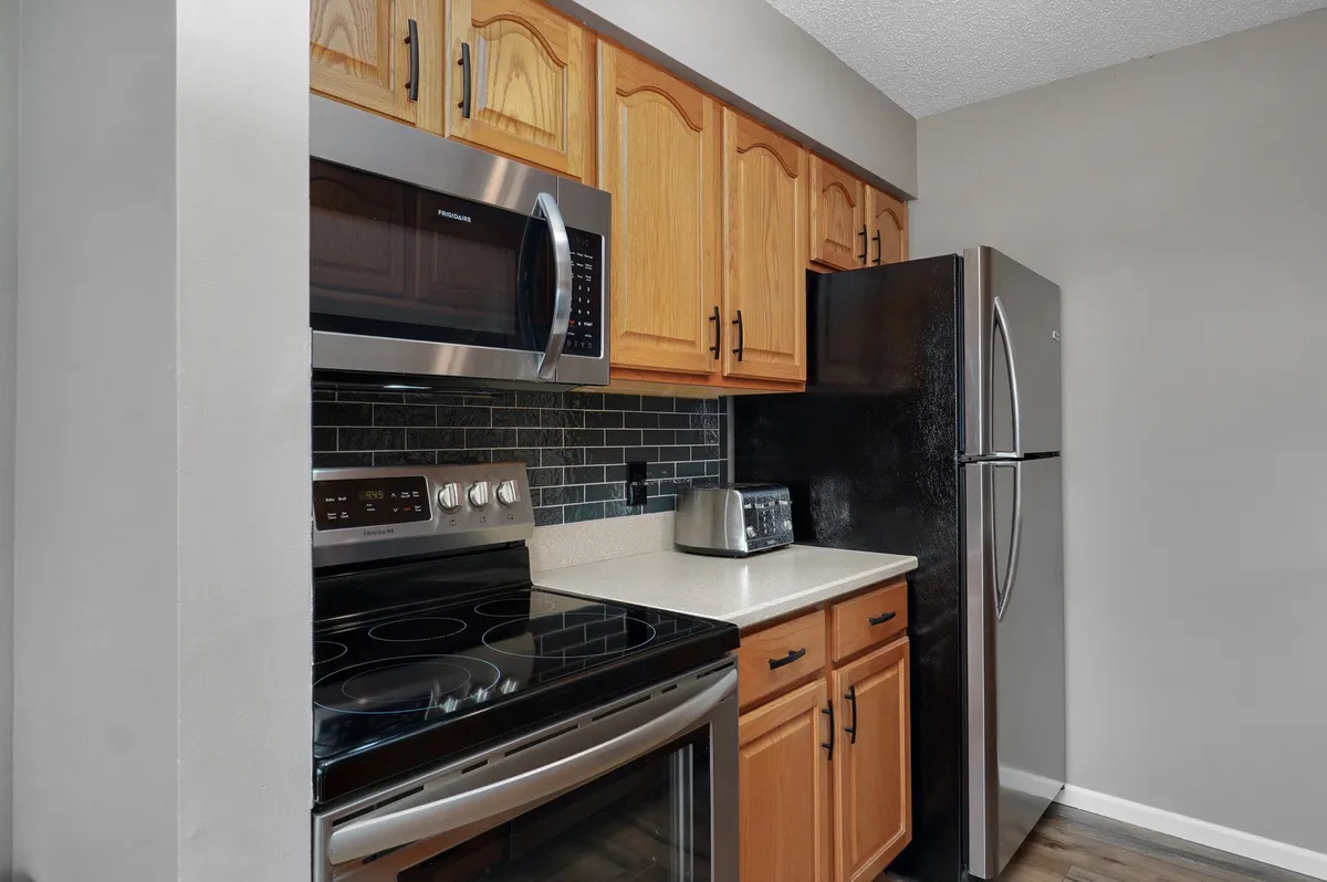 A modern kitchen with stainless steel appliances, wooden cabinets, and a black tile backsplash. The countertops offer plenty of space for meal preparation and socializing. The design is both functional and stylish, ideal for group cooking or entertaining.