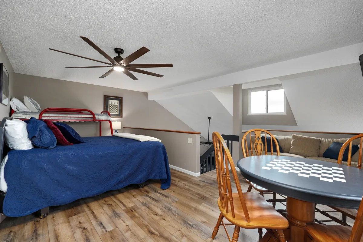 A cozy and inviting interior shot highlighting a wooden dining table set with a checkerboard for games, a comfortable bed with a blue blanket, and natural light filtering in. The space exudes a playful and relaxing atmosphere, ideal for family downtime after an exciting day out.