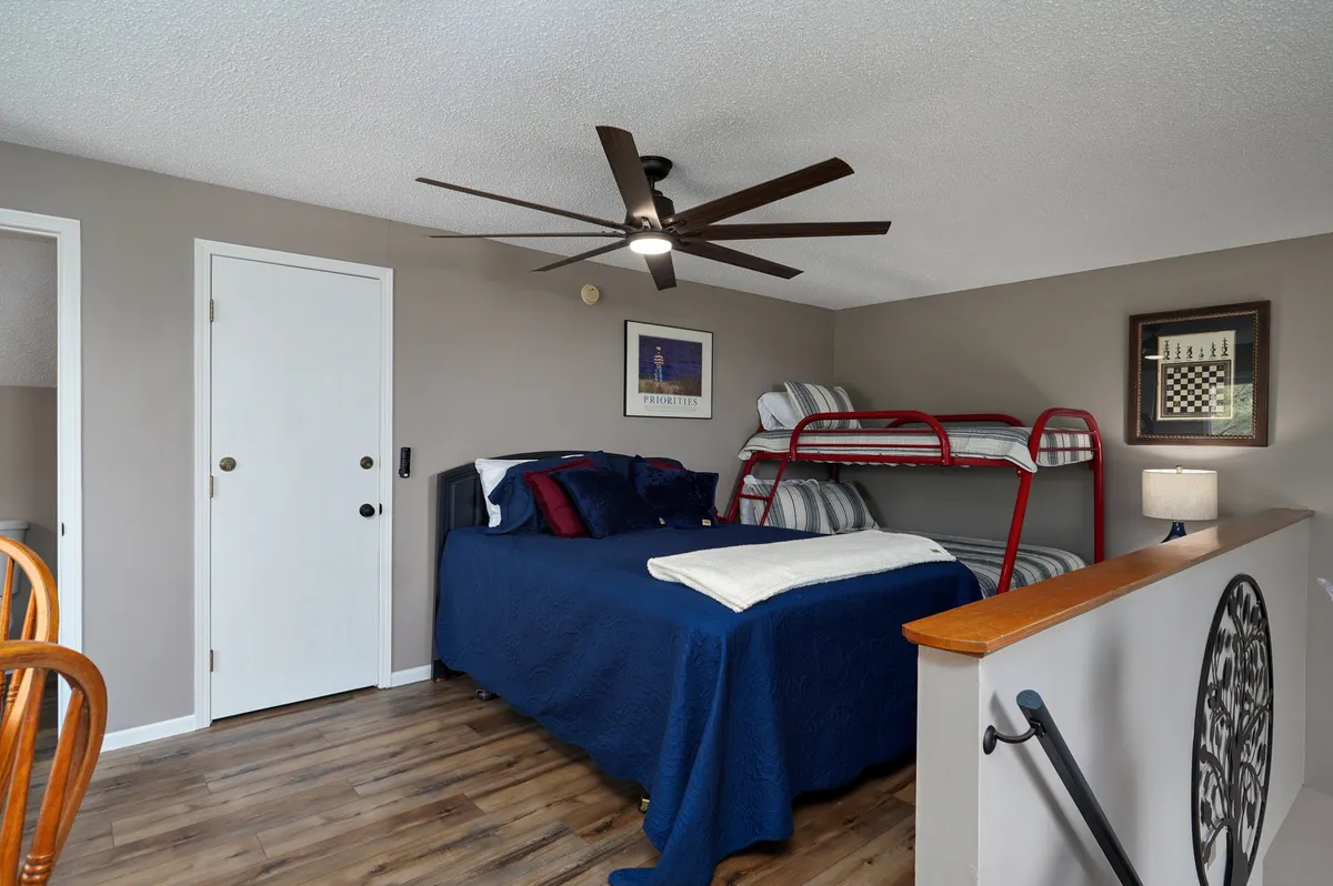 A family-friendly bedroom with a queen bed and twin-over-full bunk bed, complemented by playful wall art and a ceiling fan. The layout maximizes sleeping arrangements, showcasing a versatile space tailored for families or groups with kids.