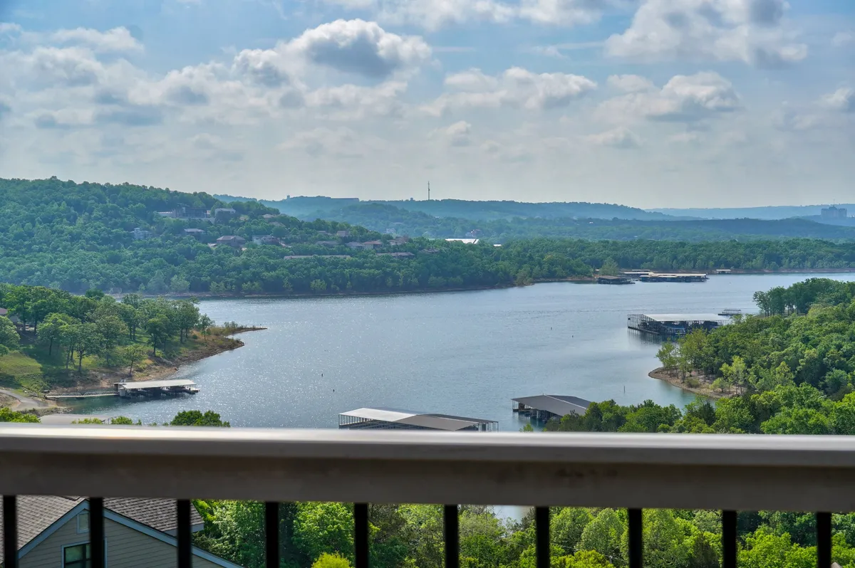 A panoramic view of a serene lake, bordered by lush green hills and distant mountains with a few boathouses dotting the shoreline. The tranquil water suggests opportunities for boating, fishing, and peaceful reflection, while the natural landscape highlights the area’s scenic beauty.