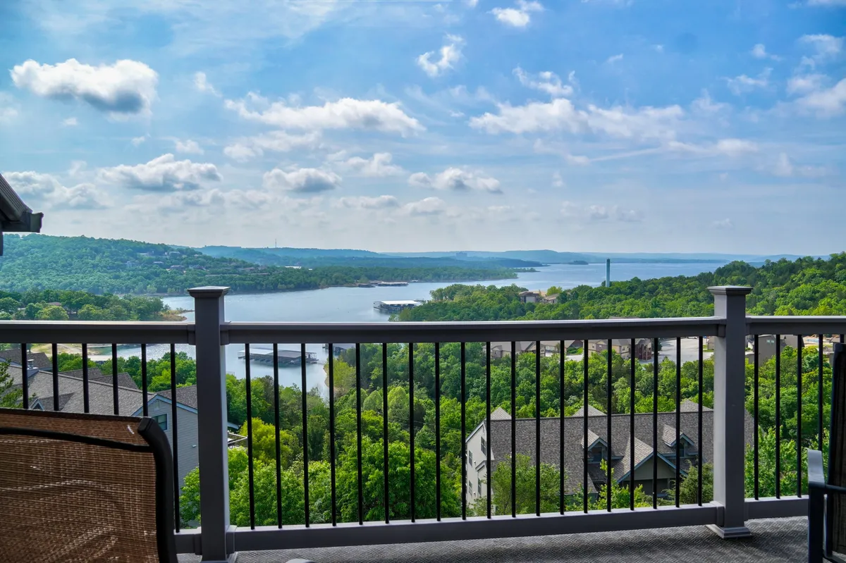 A breathtaking, wide view of Table Rock Lake, with wooded hills in the background and a cloudy sky above. The perspective makes it clear this image is taken from a balcony or deck, capturing the tranquil, natural beauty and inviting visitors to imagine outdoor relaxation and adventure.