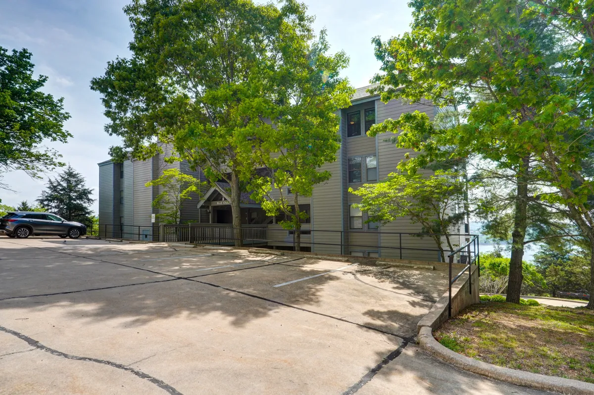 A modern building facade surrounded by beautifully maintained greenery and a convenient parking area. The entrance is welcoming, suggesting easy access for guests and a sense of arrival at a well-kept resort community.